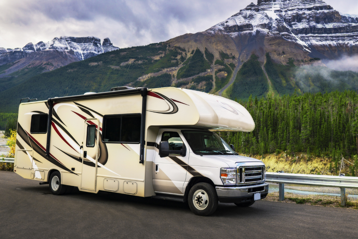 RV drives along in front of a mountain range.