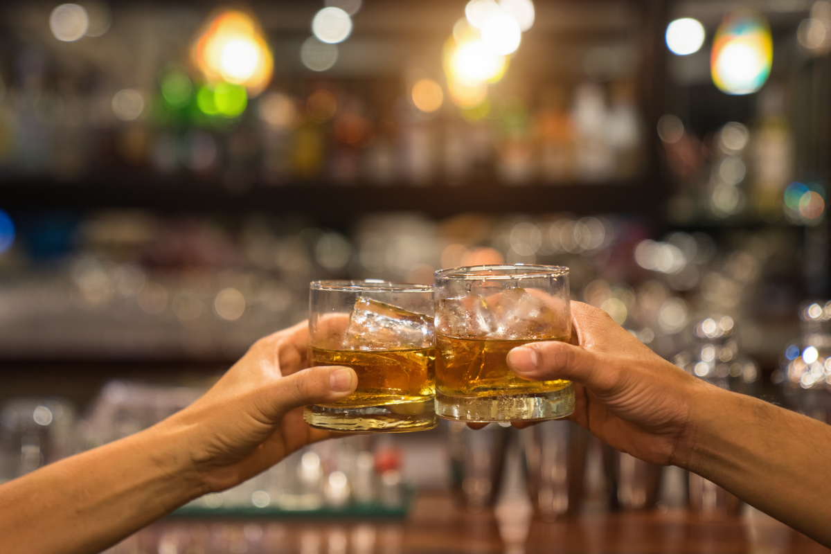 Two men clinking glasses of whiskey drink alcohol beverage together at counter in the pub