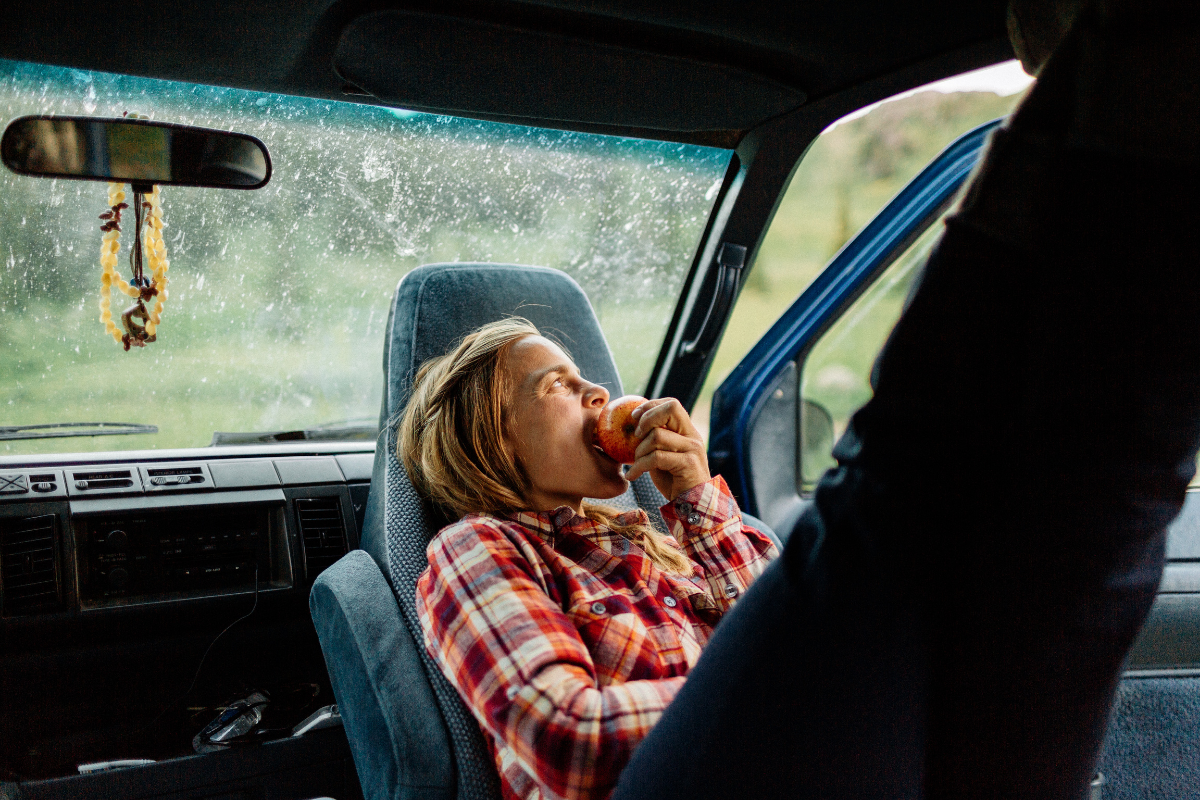 Happy woman eating an apple and looking out the door of her van as she van camps in the wilderness of Montana.