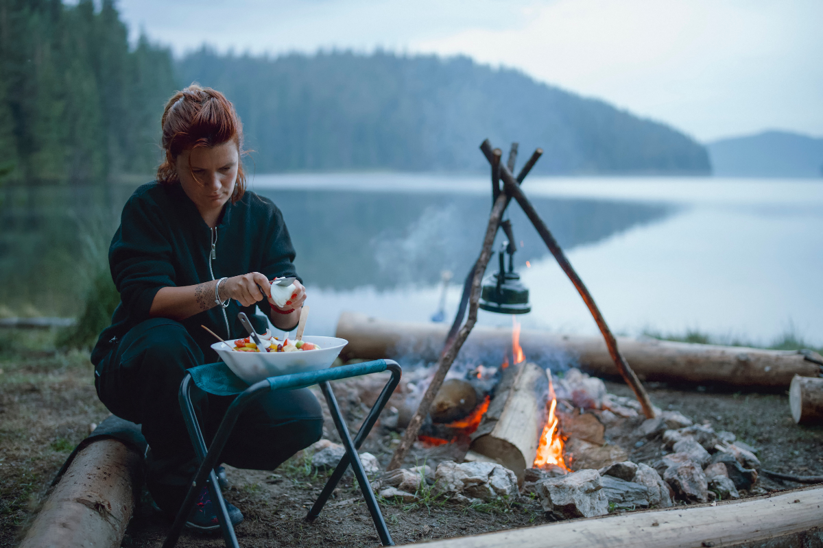 Young woman is cooking next to the campfire at the campsite