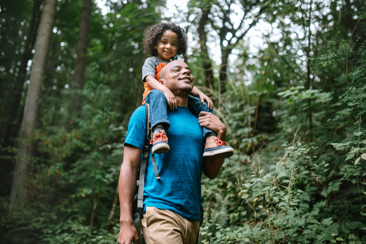 A young mixed race family spends time together outside in Washington state, enjoying the beauty of the woods in the PNW. The dad holds his boy on his shoulders.