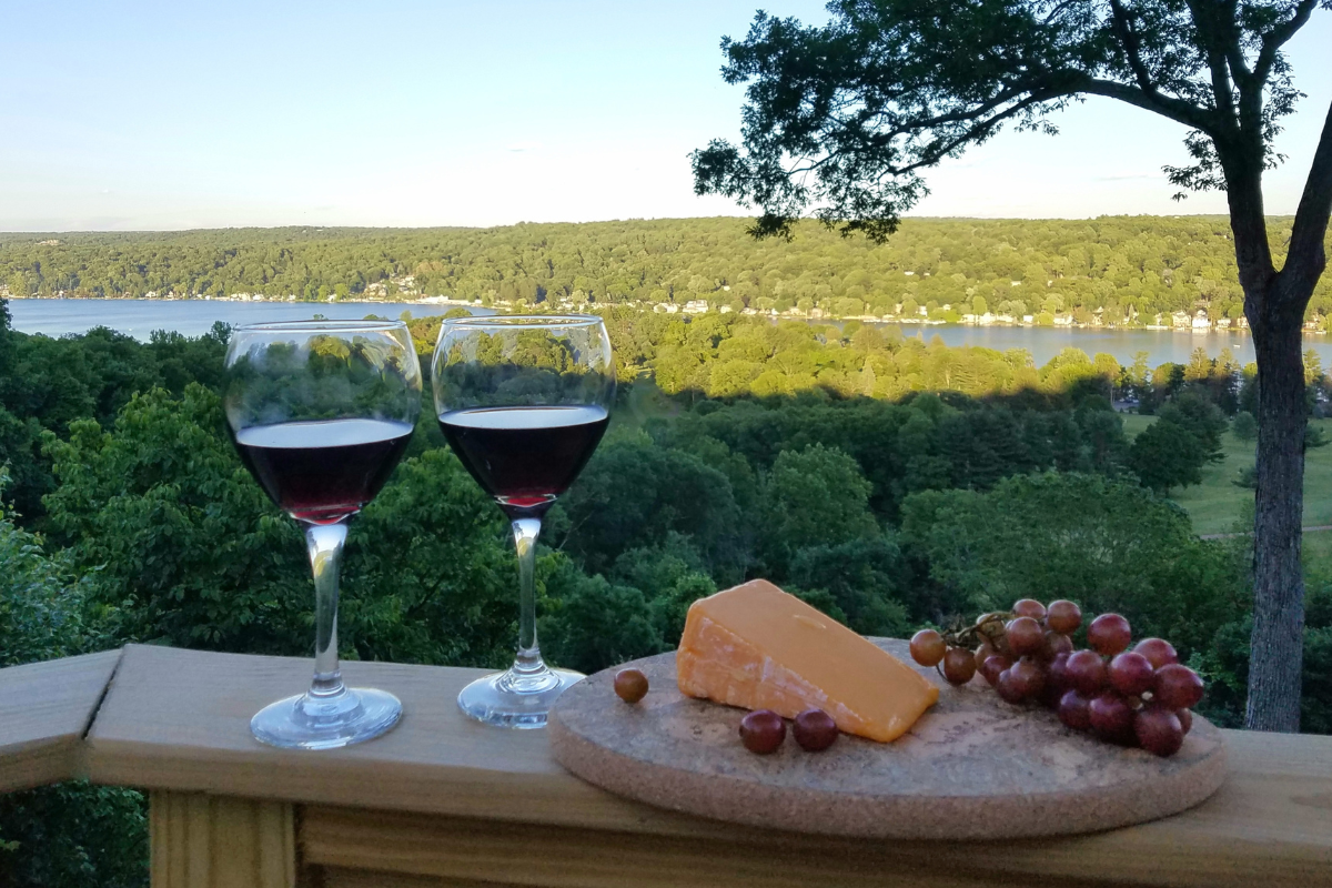 Two wine glasses filled with a Cabernet style wine with a platter of cheese and red grapes against a water background; travel and wine tasting ideas, Finger Lakes wine tours.